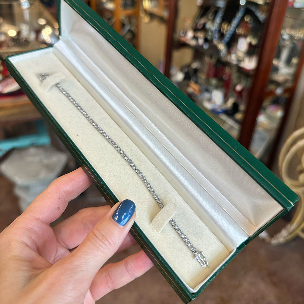 10k diamonds on silver bracelet in a green jewelry box held by a hand with blue nail polish.