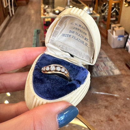 Gold ring with diamonds in a jewelry box held by a hand with blue nail polish inside of an upstate NY antique shop.