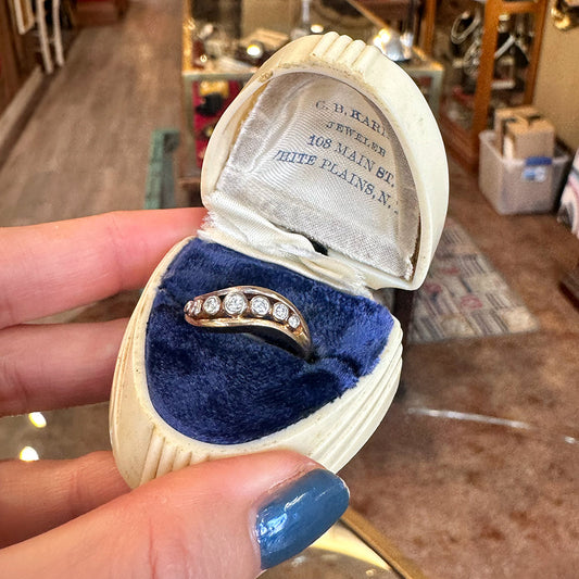 Gold ring with diamonds in a jewelry box held by a hand with blue nail polish inside of an upstate NY antique shop.