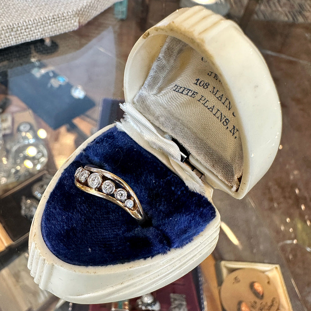 Gold ring with diamonds in an open jewelry box on a reflective surface inside of an antique shop.