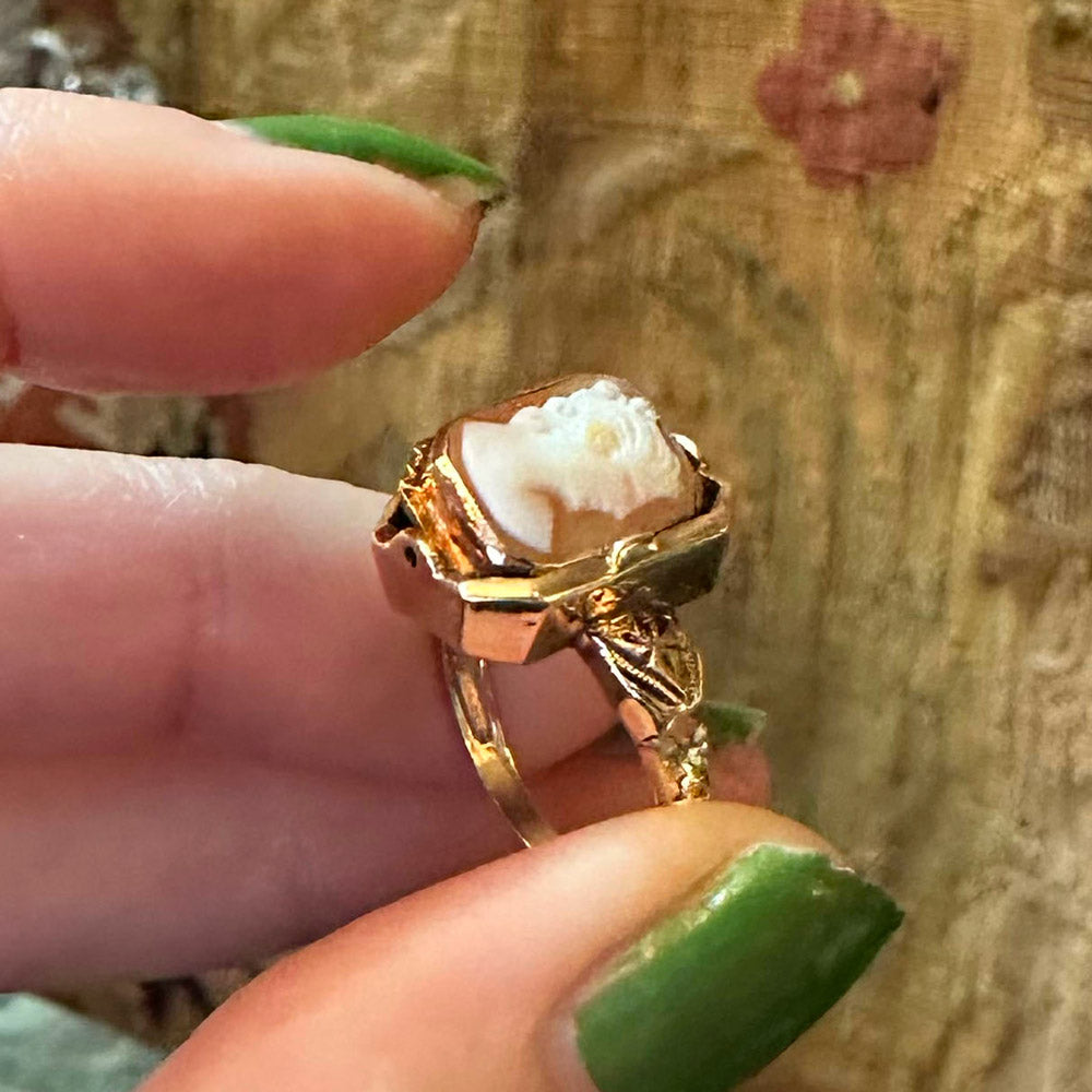 Gold ring with a white cameo held between fingers against a wooden background Upstate New York.