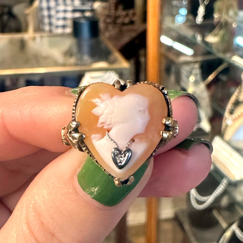 Heart-shaped cameo ring held by a hand with green nail polish in a jewelry store.