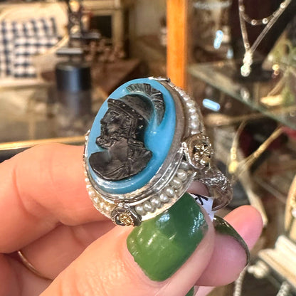 Agate and pearl Art Deco ring with blue stone and hand-carved, black face cameo held by a hand with green nail polish.