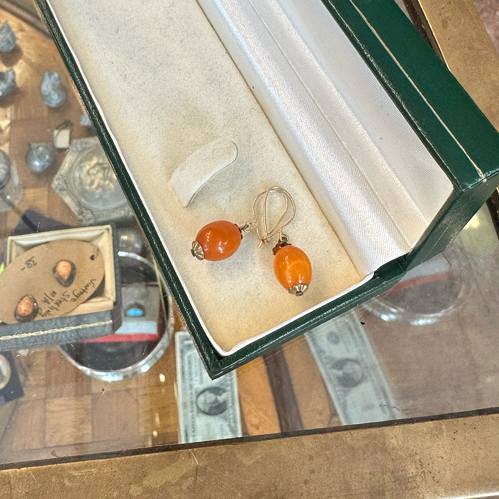 Pair of amber earrings in a jewelry box on a reflective surface inside an Antiques Center.