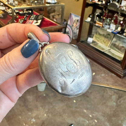 Back of a beautiful sterling silver locket with engraving held by hand inside an antique store in Saugerties New York.