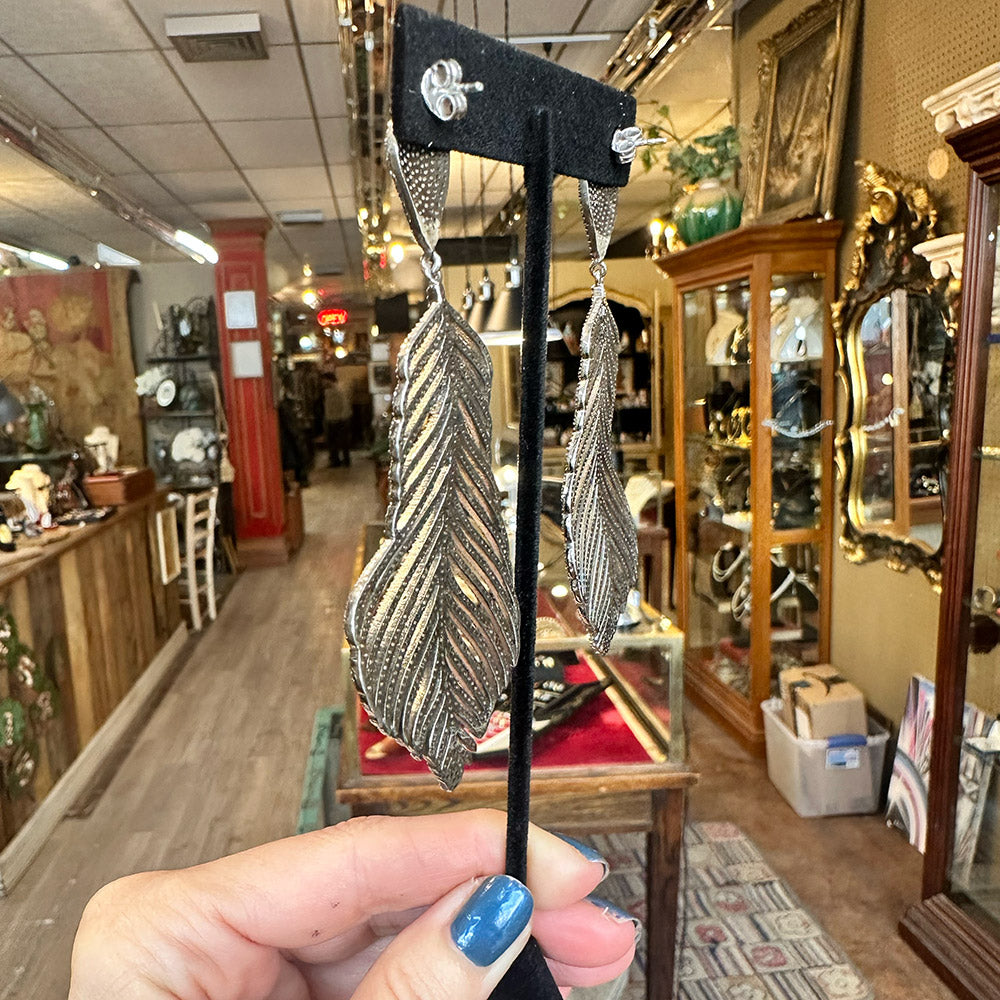 Back-view of feather-shaped earrings on a black velvet stand held in front of a store interior in Saugerties New York.