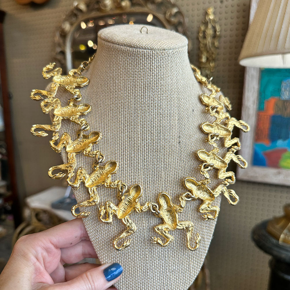 back-view of gold necklace with monkey charms on a mannequin bust, held by a hand with blue nail polish.