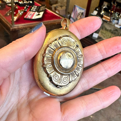 Hand holding a decorative gold locket with intricate designs inside a vintage store.