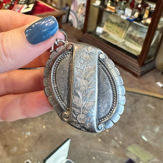 Silver victorian locket with floral designs held by a hand inside an Antique Store Upstate New York.