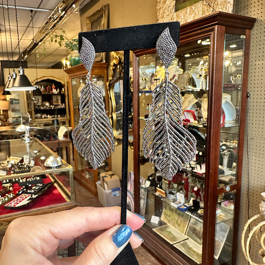 Silver sterling and black feather-shaped earrings held up in an antique shop.