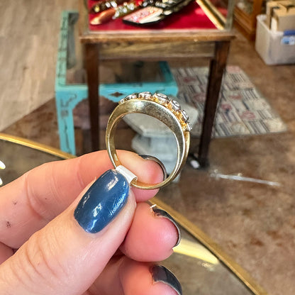 Hand holding a gold ring with diamonds against a blurred indoor background