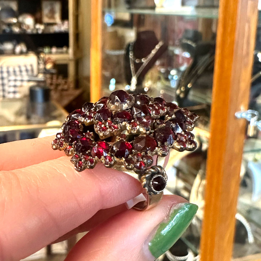 Close-up of a hand holding an antique Victorian ring with red gemstones in an antique center store.