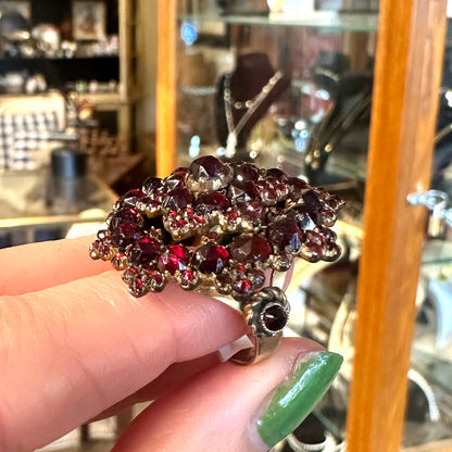 Close-up of a hand holding an antique Victorian ring with red gemstones in an antique center store.