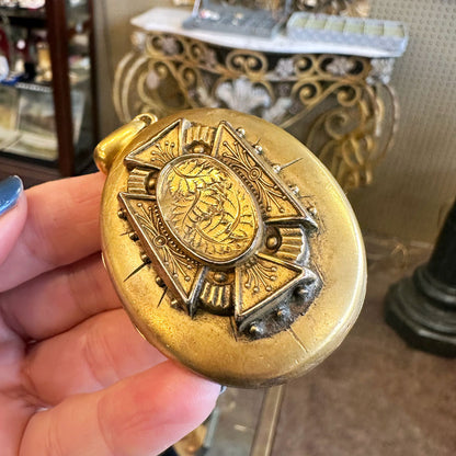 Decorative gold object held by a hand with a blurred background inside an Antique Center.