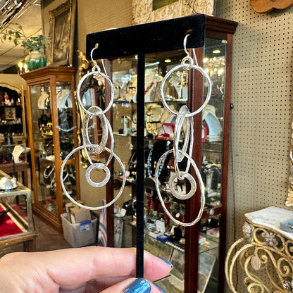 Hammered silver hoop earrings on a stand with an antique store interior in the background.
