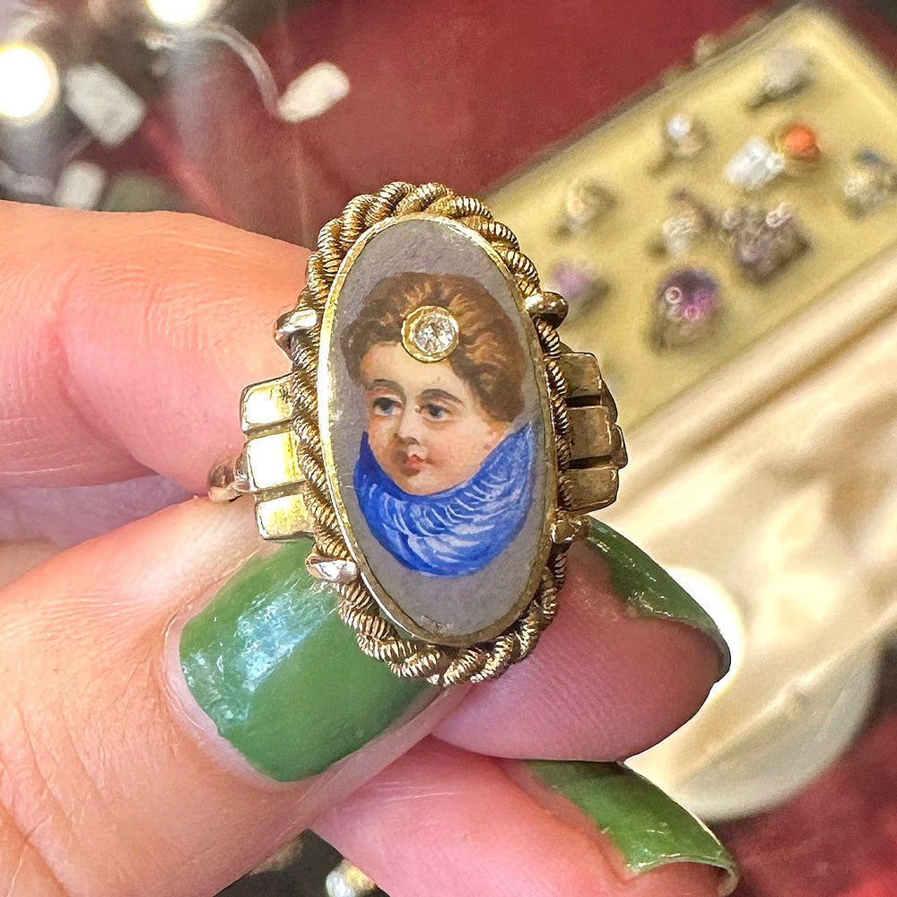 Ring with portrait from the 19th century  held by a hand with green nail polish inside of an ntique store.
