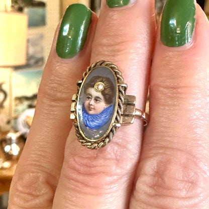 Ring with portrait miniature on a finger with green nail polish inside of an antique store.