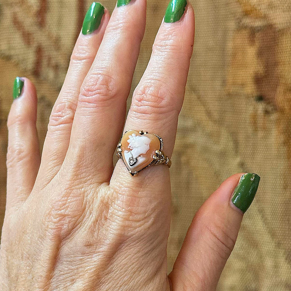 Hand model wearing a vintage-style ring with a large stone against a textured background inside an antique shopping center.