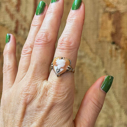 Hand model wearing a vintage-style ring with a large stone against a textured background inside an antique shopping center.
