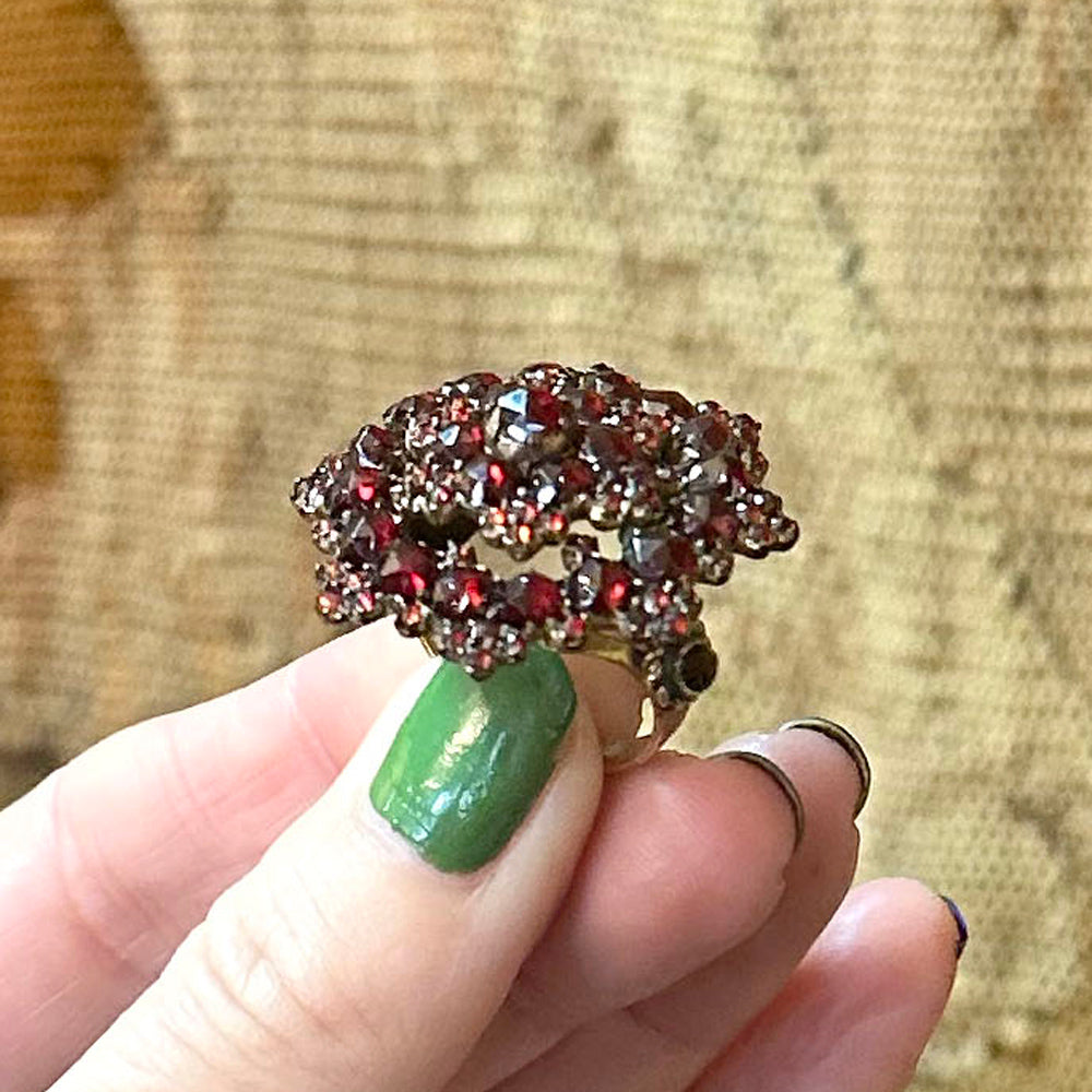 Decorative ring with red gemstones held by a hand with green nail polish on a textured background Upstate New York.