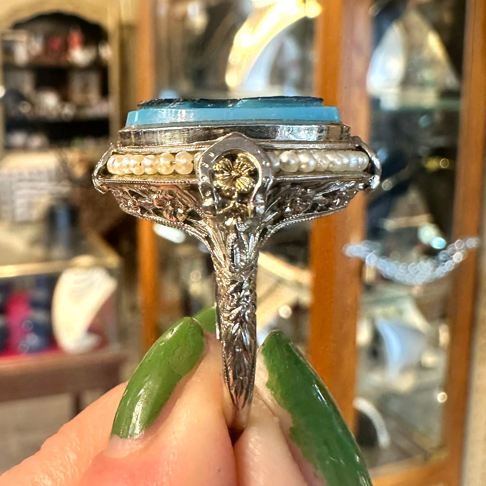 Side of a beautiful art deco ring in yellow and white gold held up- howing metal carvings inside of an antique store.