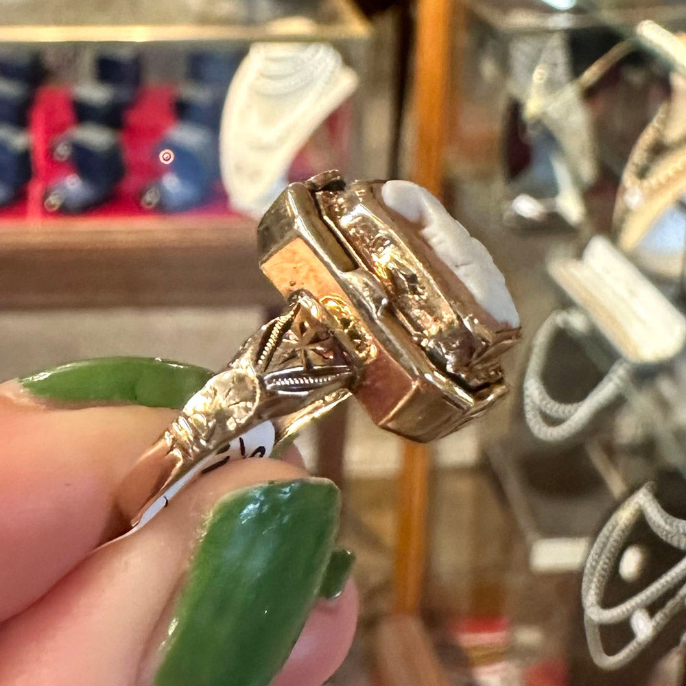 Gold ring with intricate design held by a hand with green nail polish, blurred background Upstate New York.
