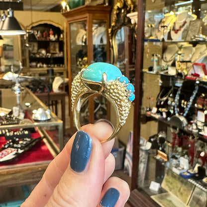 Gold Mid-century ring with turquoise stones held by a hand in an antique jewelry store.