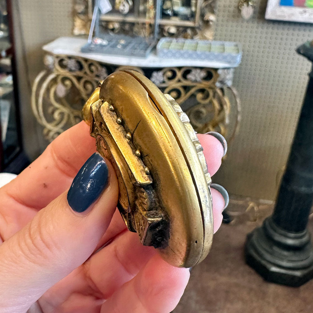 Hand holding a gold locket with intricate details in an indoor setting Upstate NY.
