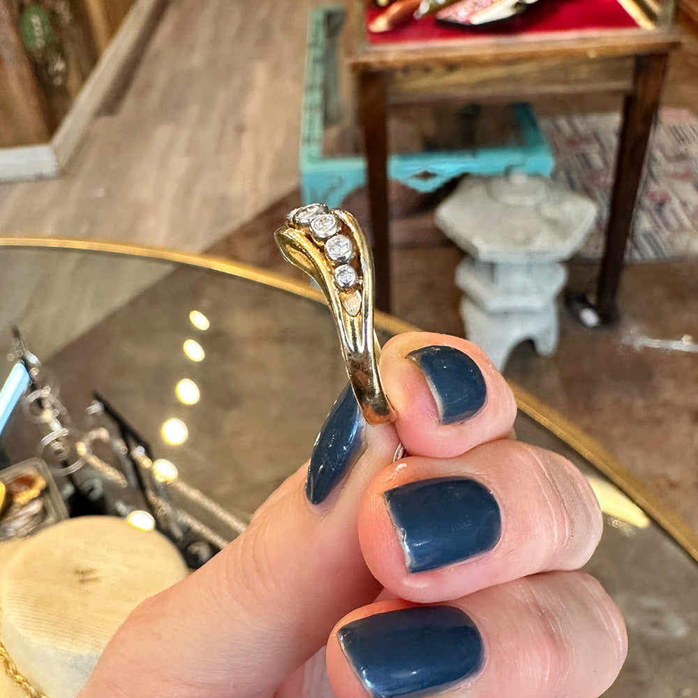 Gold ring with diamonds held by a hand with blue nail polish inside of an Antiques shop.