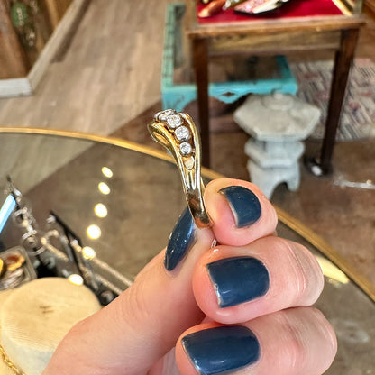 Gold ring with diamonds held by a hand with blue nail polish inside of an Antiques shop.
