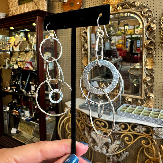 Hammered silver hoop earrings on a display stand inside an antique store.
