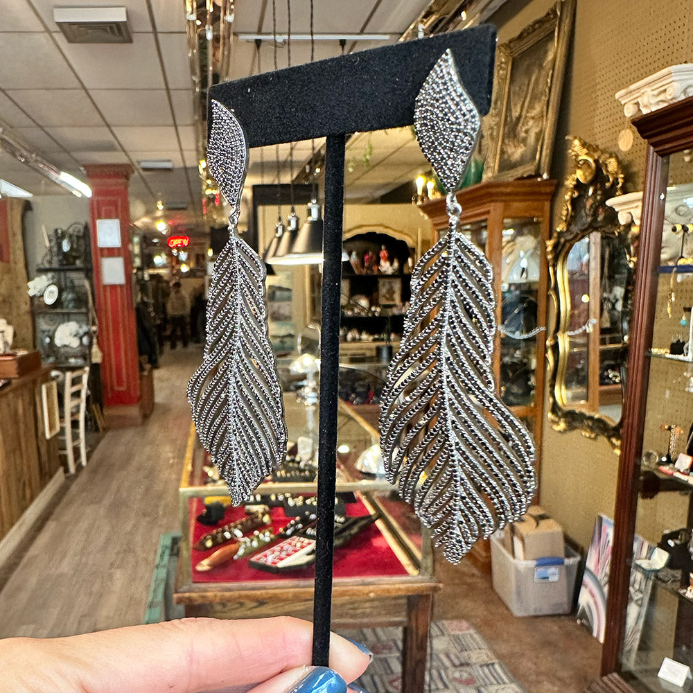 Pair of black and sterling silver feather-shaped earrings on a black stand held up inside an Antique store Upstate NY.
