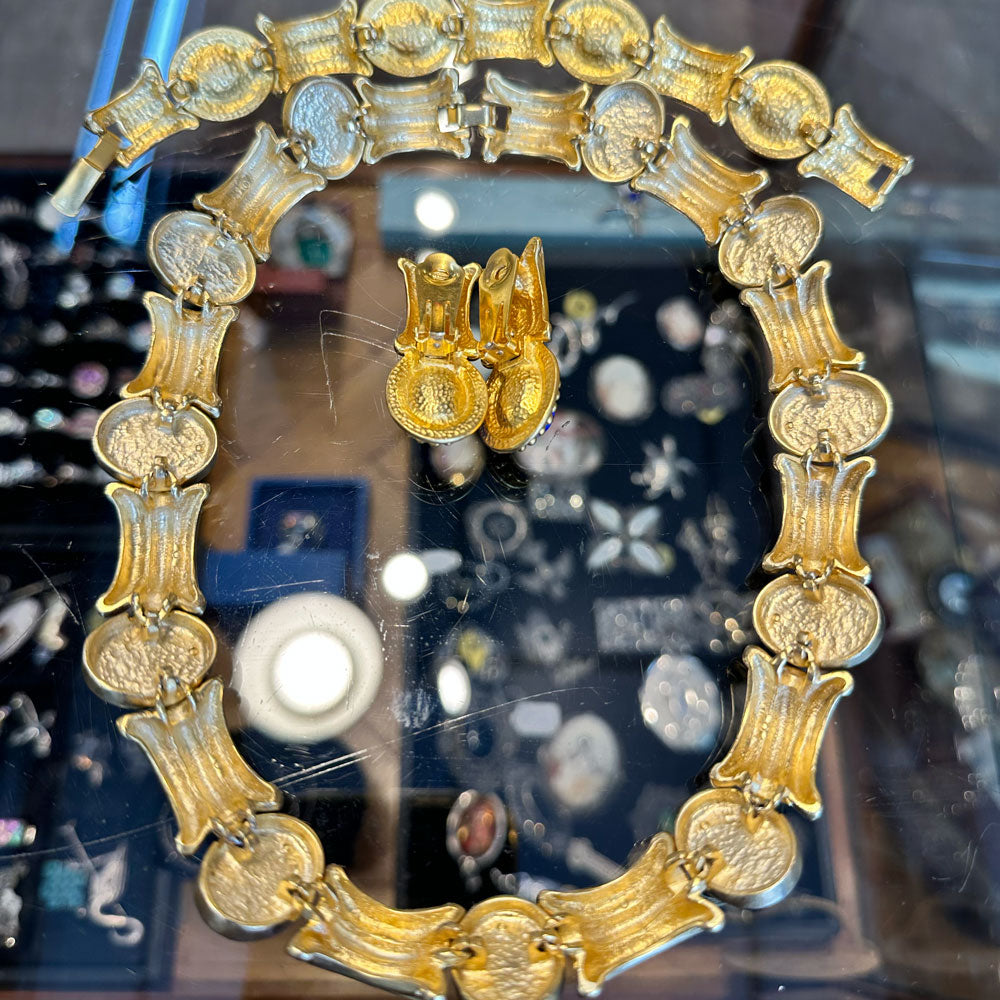 Back of a gold necklace, bracelet, and earrings set from the 80s laying flat on a glass jewelry case in an antique store.