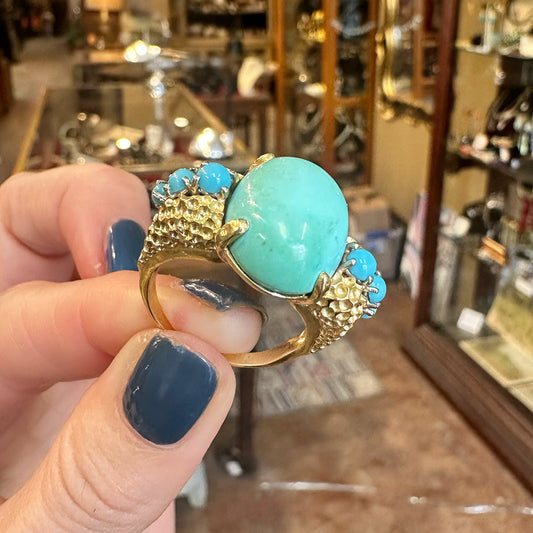 Turquoise statement ring with gold accents held by a hand in an antique store Upstate New York.