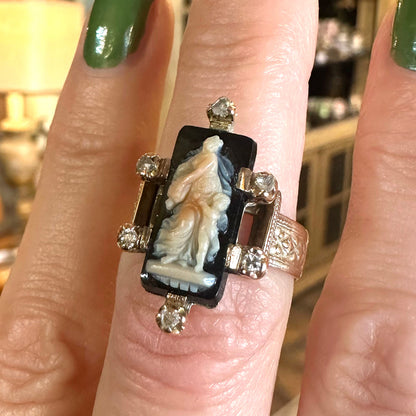 Ring with a detailed design on a finger, set against a blurred indoor background in an antique shopping center.