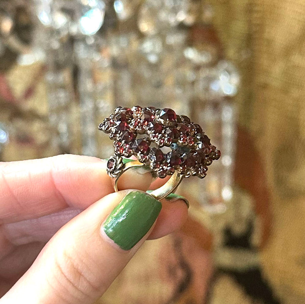 Close-up of a hand holding a Victorian bohemian ring with gemstones against a blurred background.