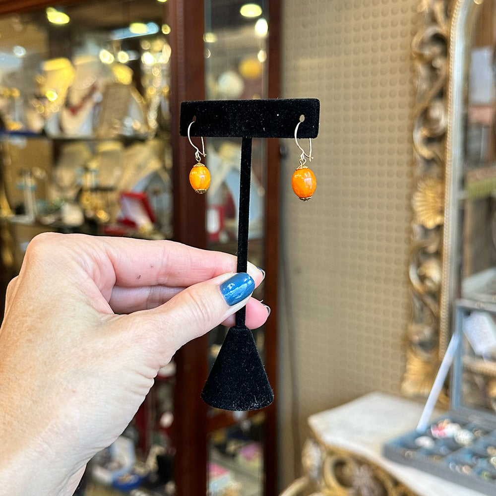 Hand holding a black, velvet earring stand with amber/orange and gold earrings in an antique center.